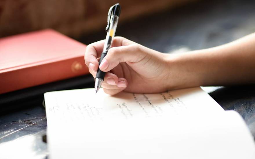 Une main écrit au stylo sur une feuille
