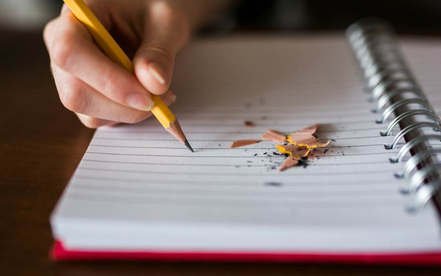 Une main écrit au crayon dans un carnet