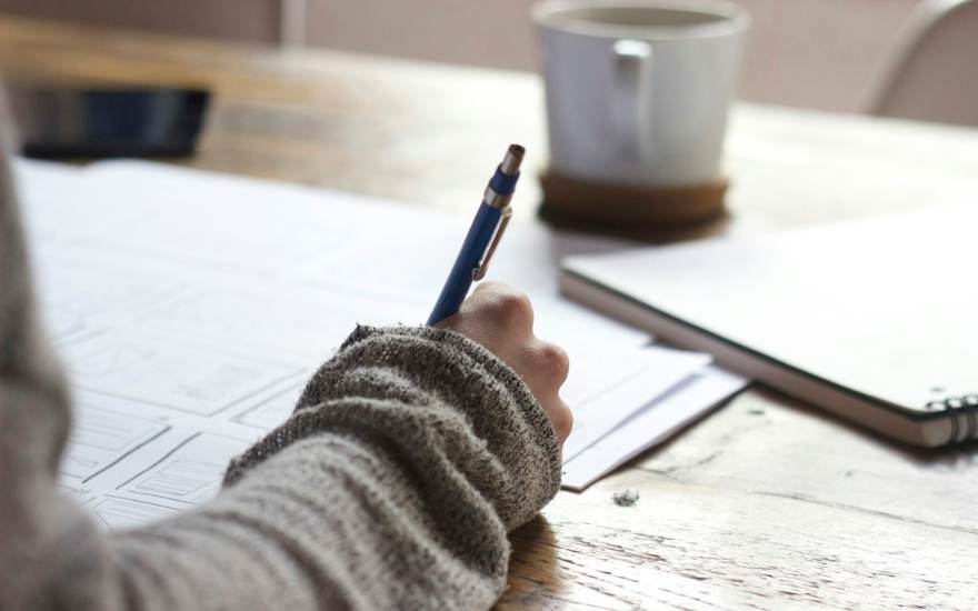Une personne prend des notes, une tasse à côté